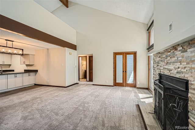 unfurnished living room with light carpet, beam ceiling, a fireplace, high vaulted ceiling, and baseboards
