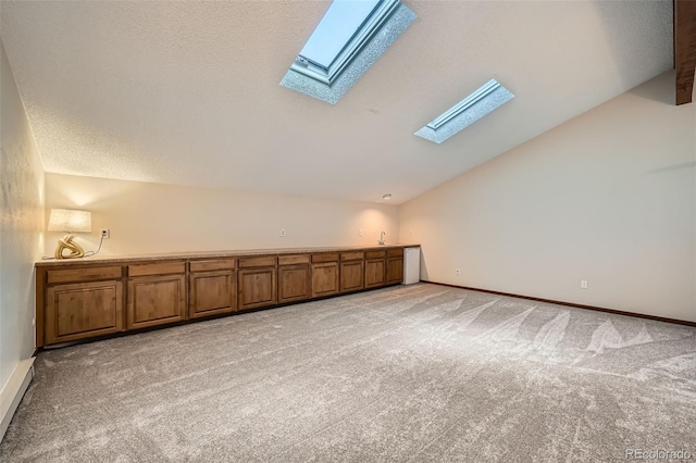 bonus room featuring vaulted ceiling with skylight, baseboards, a textured ceiling, and light colored carpet