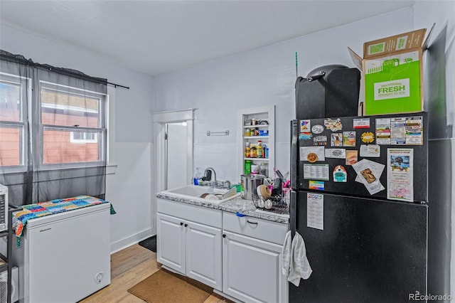 kitchen featuring a sink, freestanding refrigerator, white fridge, white cabinets, and light wood finished floors