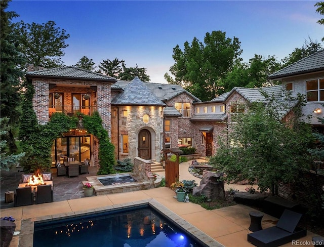 850 E Radcliff Ave, Cherry Hills Village, CO 80113 - back of property at dusk featuring a patio area, an outdoor pool, an outdoor living space with a fire pit, brick siding, and stone siding