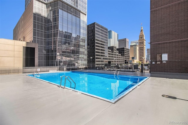 community pool with a view of city, a patio, and fence