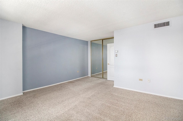 empty room with carpet, a textured ceiling, visible vents, and baseboards