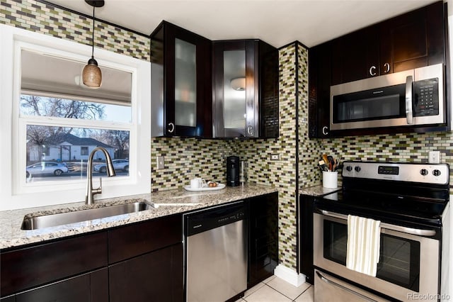 kitchen featuring appliances with stainless steel finishes, light stone counters, sink, decorative light fixtures, and backsplash