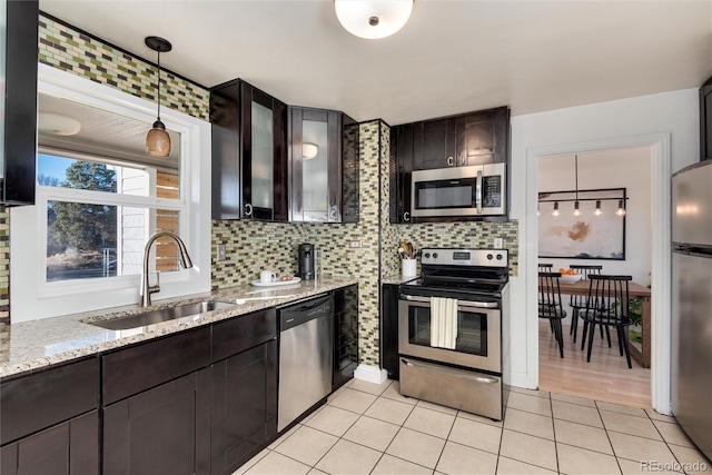 kitchen with light tile patterned floors, decorative light fixtures, a sink, stainless steel appliances, and backsplash