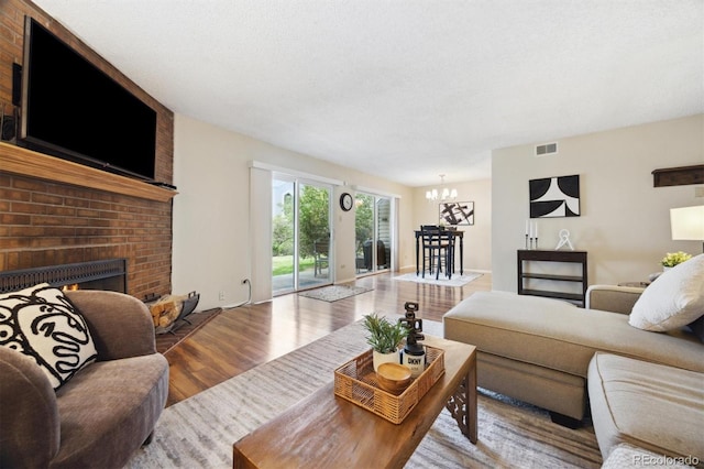 living room featuring an inviting chandelier, wood-type flooring, a fireplace, and a textured ceiling