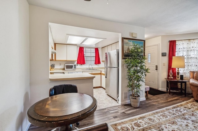 kitchen featuring sink, white cabinetry, appliances with stainless steel finishes, kitchen peninsula, and hardwood / wood-style flooring