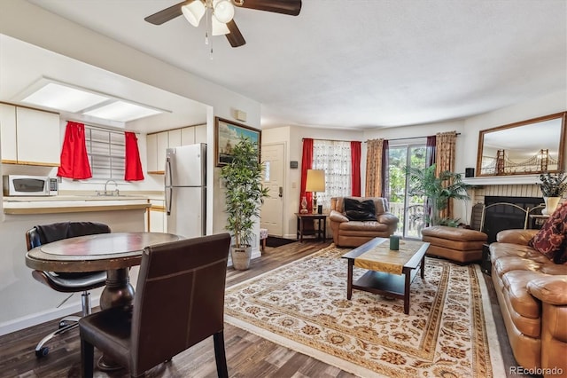 living room featuring wood-type flooring, a brick fireplace, sink, and ceiling fan