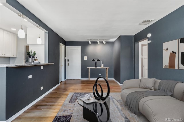 living room with light wood-type flooring, rail lighting, visible vents, and baseboards