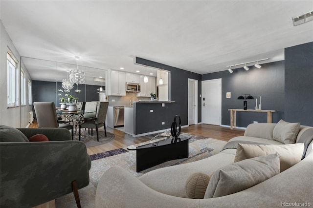 living room featuring light wood-type flooring, rail lighting, visible vents, and baseboards