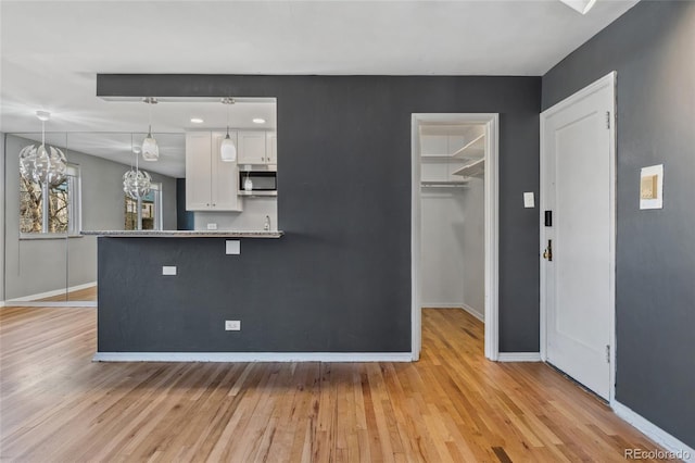 kitchen featuring baseboards, stainless steel microwave, light wood-style flooring, and white cabinets