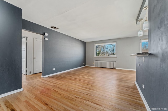 unfurnished living room featuring radiator, baseboards, visible vents, and wood finished floors