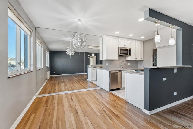 kitchen with appliances with stainless steel finishes, radiator heating unit, light wood-style flooring, and white cabinetry