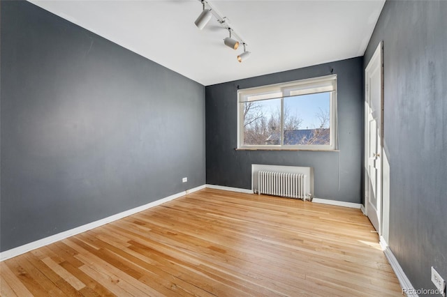 empty room with rail lighting, radiator heating unit, baseboards, and light wood-style flooring