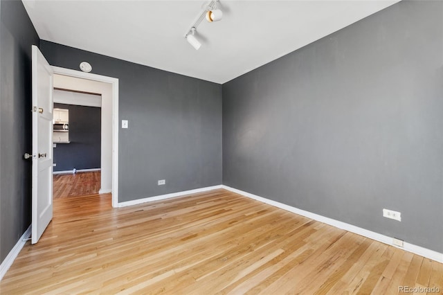 empty room featuring baseboards, track lighting, and wood finished floors