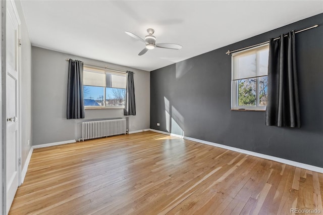 empty room featuring hardwood / wood-style flooring, radiator heating unit, baseboards, and ceiling fan