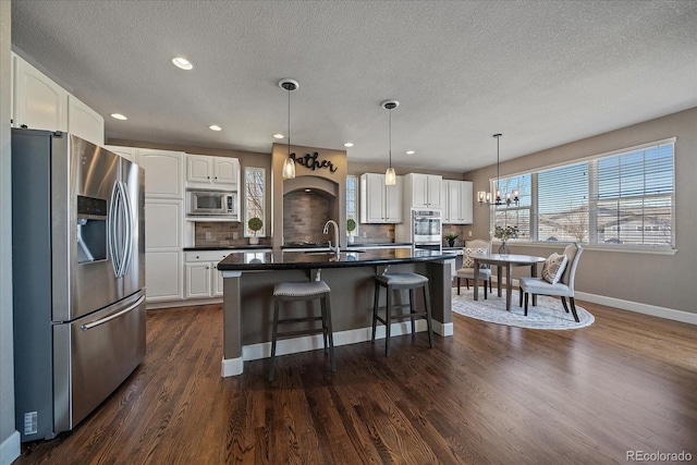 kitchen with white cabinets, dark hardwood / wood-style flooring, stainless steel appliances, and an island with sink