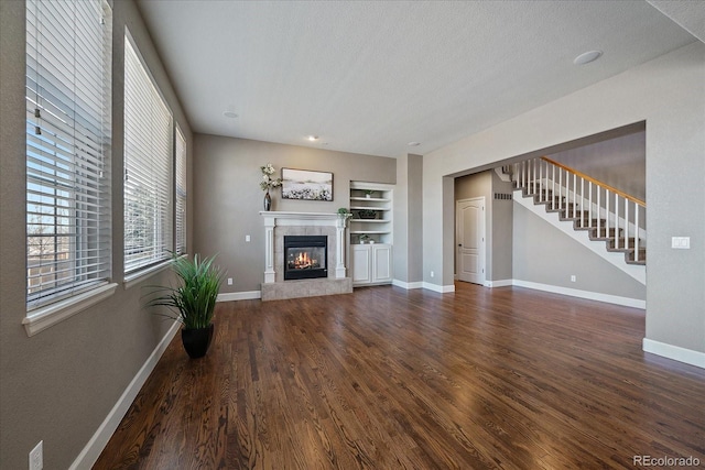 unfurnished living room with a textured ceiling, dark wood-type flooring, built in shelves, and a fireplace