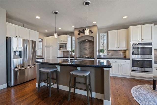 kitchen with appliances with stainless steel finishes, plenty of natural light, a center island with sink, and white cabinetry