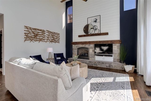 living area featuring a high ceiling, a stone fireplace, and dark wood-style flooring