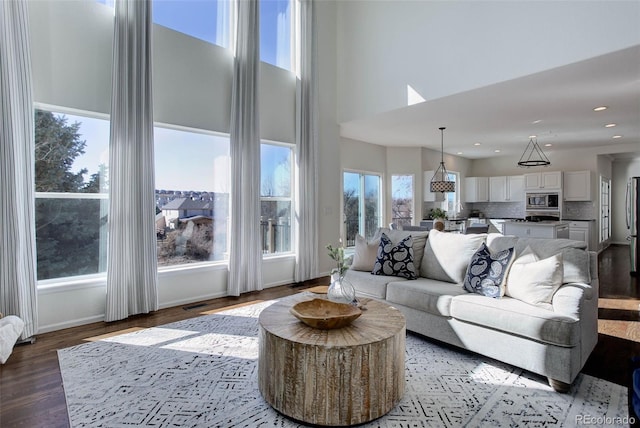 living area featuring visible vents, wood finished floors, recessed lighting, baseboards, and a towering ceiling