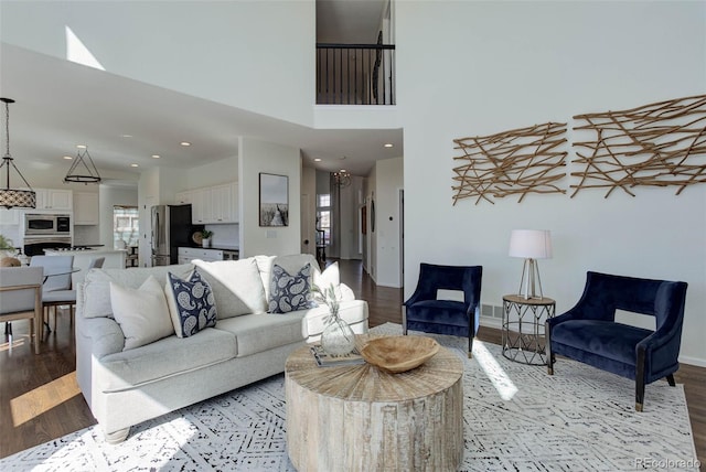 living area featuring a high ceiling, recessed lighting, baseboards, and light wood finished floors