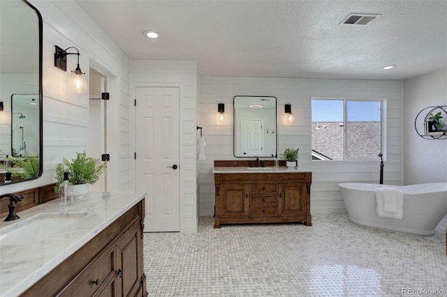 bathroom featuring visible vents, two vanities, a sink, a textured ceiling, and a soaking tub