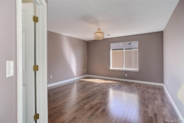 unfurnished room featuring visible vents, a notable chandelier, wood finished floors, and baseboards