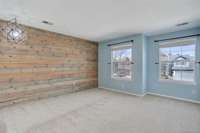 carpeted spare room featuring visible vents, wood walls, and baseboards