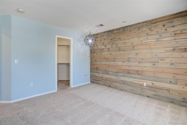 empty room with carpet, baseboards, visible vents, wood walls, and a textured ceiling