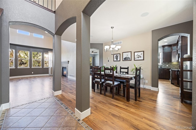 dining room with a notable chandelier, visible vents, baseboards, light wood-style floors, and a glass covered fireplace