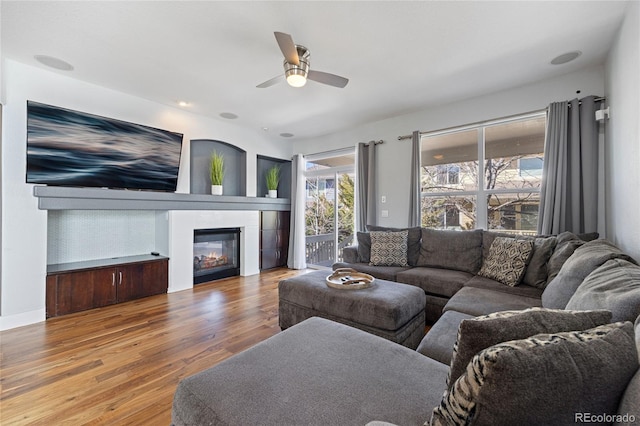 living room featuring a glass covered fireplace, wood finished floors, and a ceiling fan