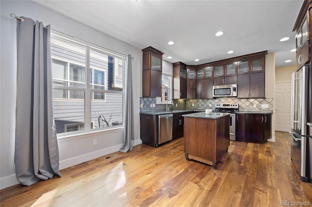 kitchen with appliances with stainless steel finishes, a kitchen island, light wood-style flooring, and tasteful backsplash