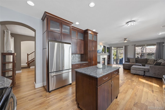 kitchen featuring arched walkways, a center island, stainless steel appliances, tasteful backsplash, and light wood-type flooring