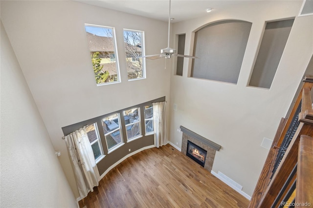 living room with visible vents, baseboards, a glass covered fireplace, ceiling fan, and wood finished floors