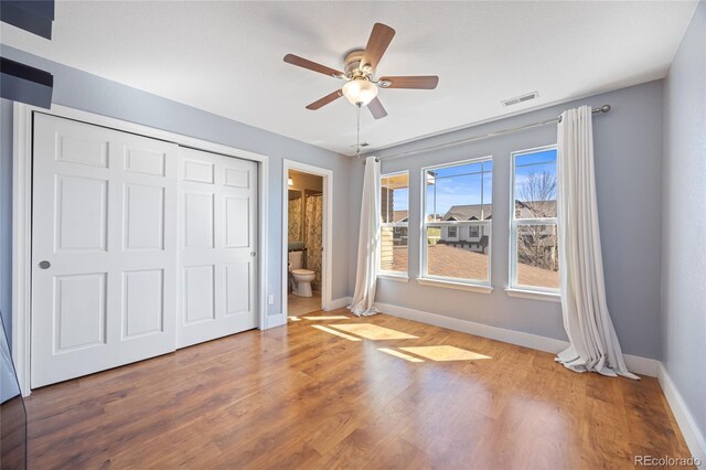 unfurnished bedroom featuring ensuite bathroom, wood finished floors, a ceiling fan, baseboards, and a closet