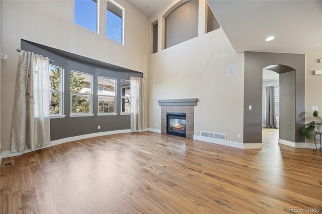 unfurnished living room featuring arched walkways, a tiled fireplace, wood finished floors, and visible vents