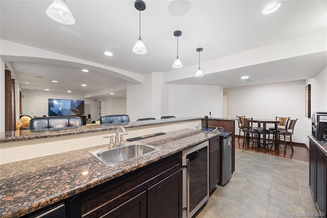 kitchen featuring beverage cooler, decorative light fixtures, a sink, and dark stone countertops