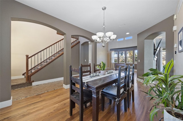 dining room with baseboards, arched walkways, stairway, wood finished floors, and an inviting chandelier