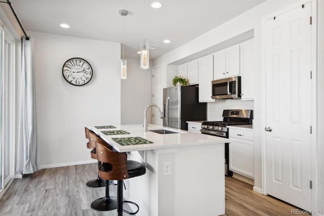 kitchen with pendant lighting, an island with sink, sink, white cabinets, and stainless steel appliances