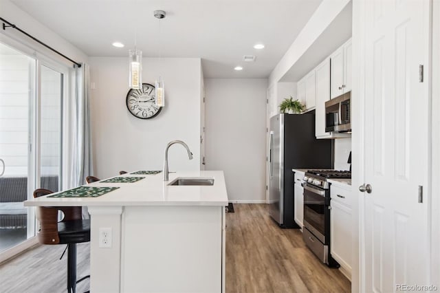 kitchen featuring sink, white cabinetry, appliances with stainless steel finishes, pendant lighting, and a kitchen island with sink