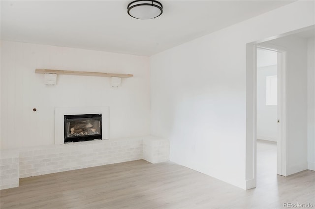 unfurnished living room with a brick fireplace and light hardwood / wood-style flooring