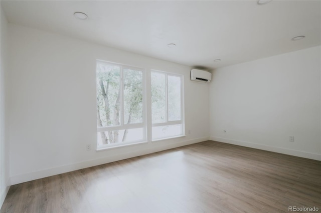 unfurnished room featuring hardwood / wood-style flooring, a healthy amount of sunlight, and a wall mounted air conditioner