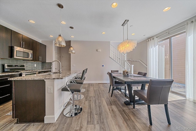 21392 E Stroll Ave, Parker, CO 80138 - kitchen with appliances with stainless steel finishes, a kitchen breakfast bar, wood finished floors, tasteful backsplash, and recessed lighting