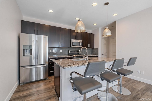 21392 E Stroll Ave, Parker, CO 80138 - kitchen featuring stainless steel appliances, tasteful backsplash, a kitchen bar, an island with sink, and dark wood-style flooring