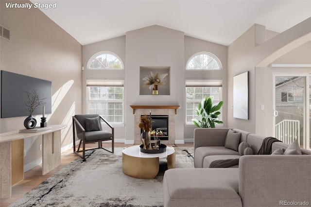 living room featuring light hardwood / wood-style floors, plenty of natural light, a tile fireplace, and high vaulted ceiling