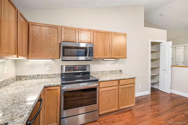 kitchen featuring dark wood-type flooring, light stone countertops, appliances with stainless steel finishes, and vaulted ceiling