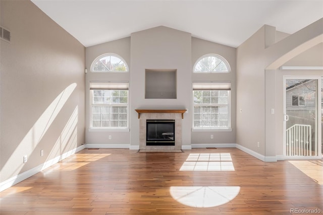 unfurnished living room featuring light hardwood / wood-style floors, a tiled fireplace, and high vaulted ceiling