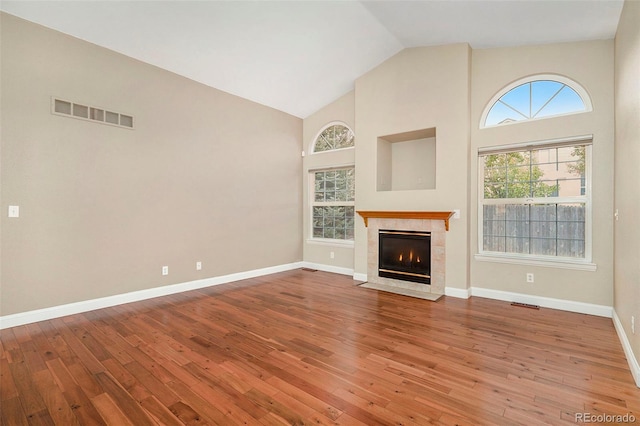 unfurnished living room with a fireplace, a wealth of natural light, wood-type flooring, and high vaulted ceiling