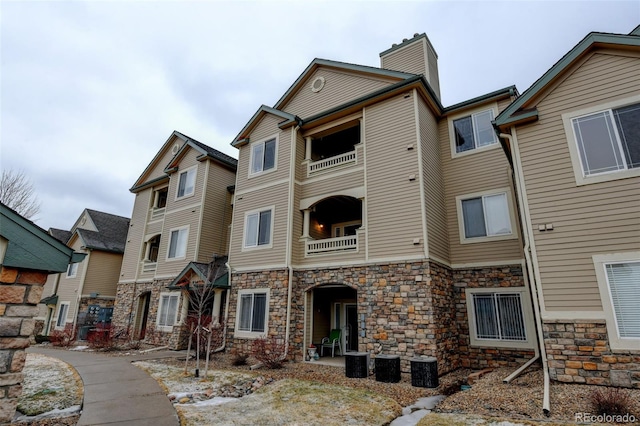 view of front of house with central air condition unit, stone siding, a balcony, and a chimney