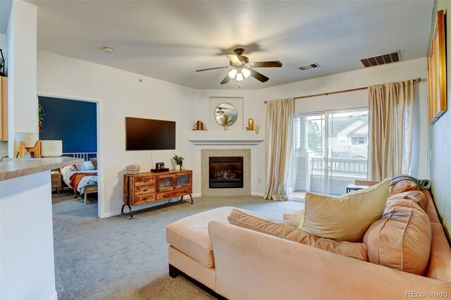 living area featuring a tiled fireplace, a ceiling fan, visible vents, and light carpet